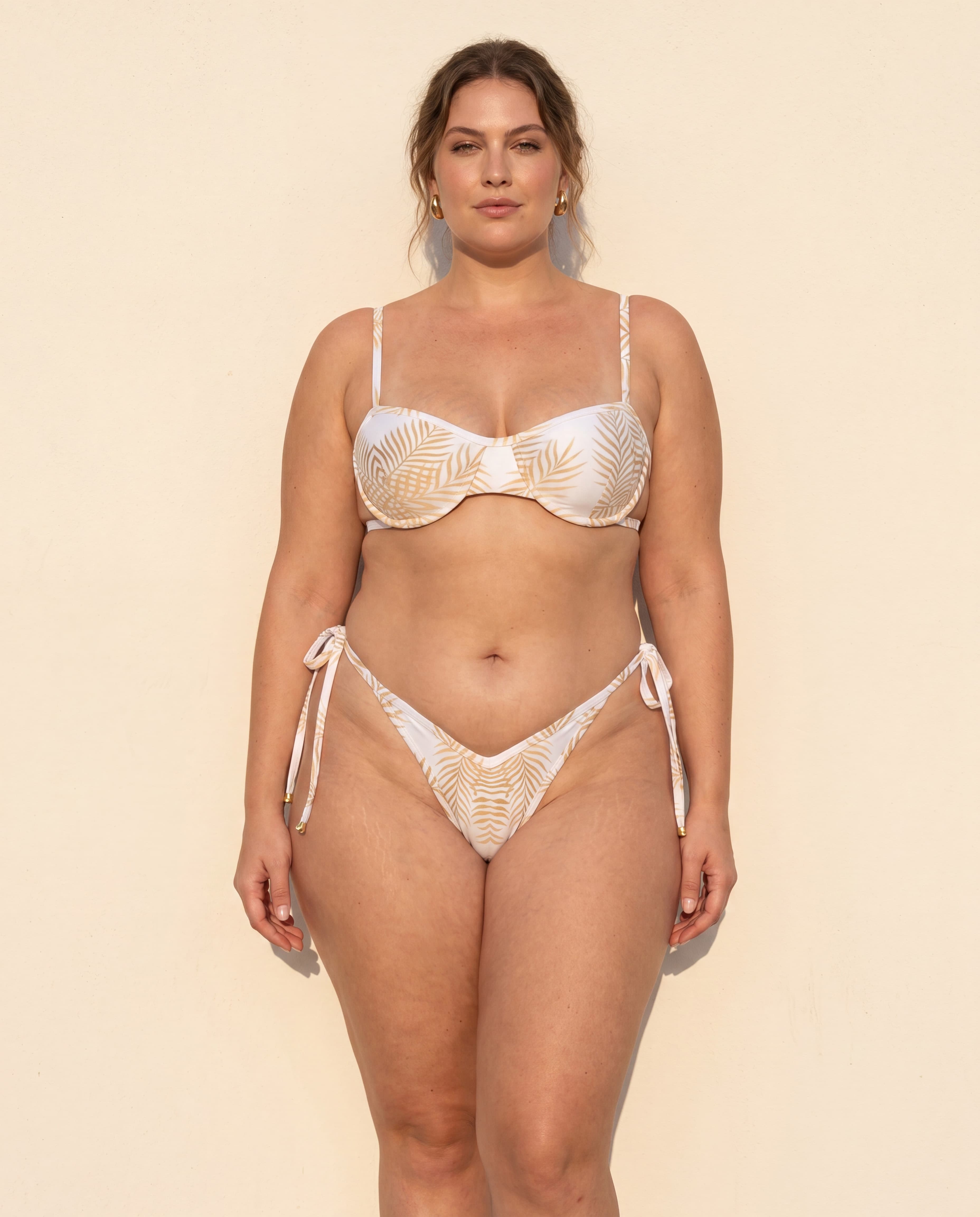 Mujer curvy en bikini Cannes Lumière blanco con estampado de hojas de palmera doradas y top balconette, colección Riviera de Leonika Swimwear