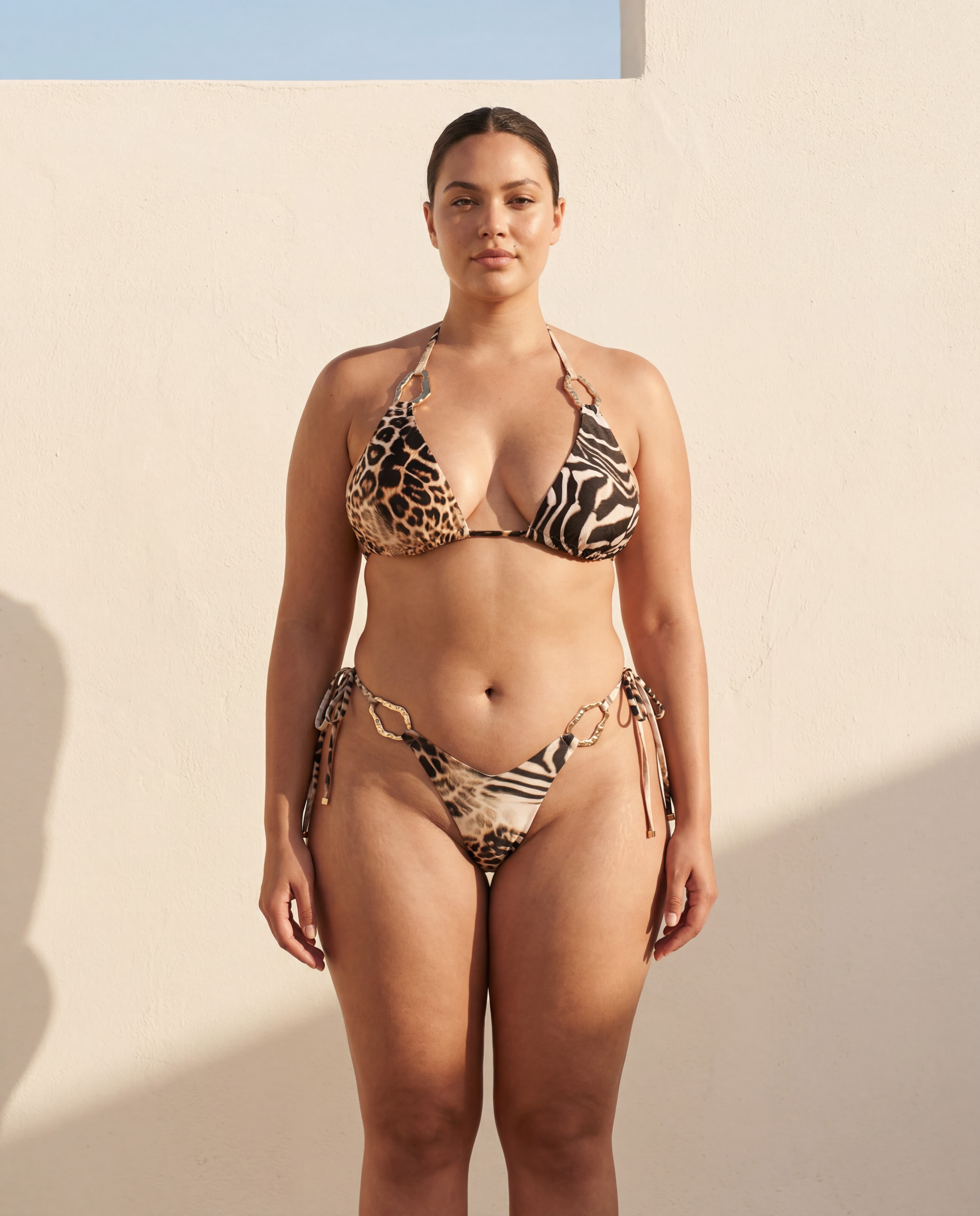 Mujer curvy en bikini Mónaco Savage de estampado leopardo y cebra con aros dorados, frente a un muro encalado, colección Riviera de Leonika Swimwear